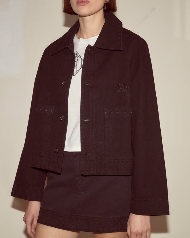 A person wearing an Embroidered Denim Jacket - Black over a white shirt and black skirt, standing against a plain background.