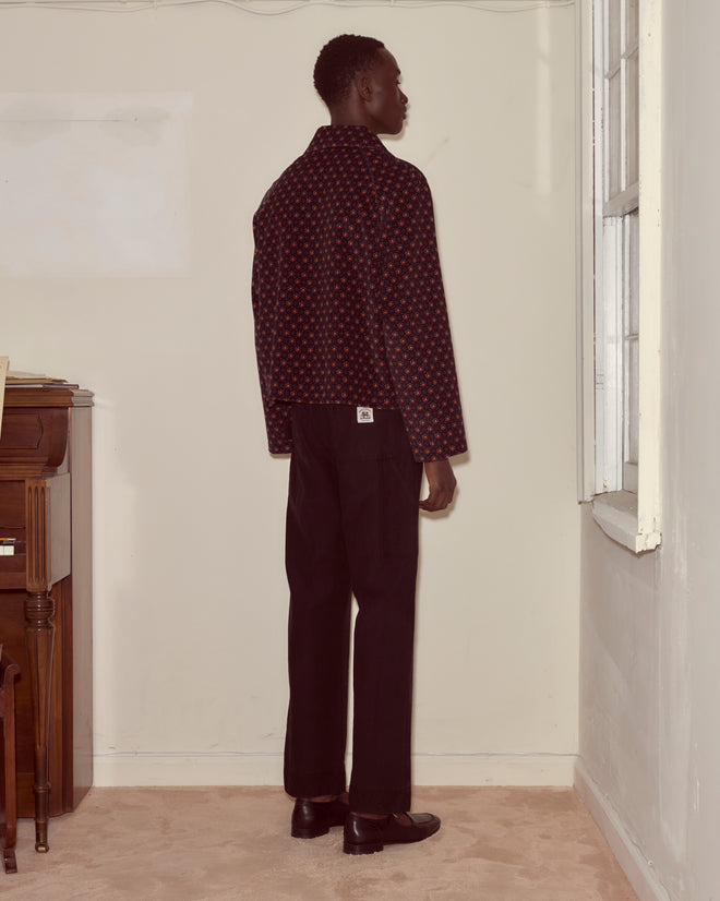 A person in dark clothing and a McAllister Corduroy Jacket stands in a corner, facing a window, seen from behind.