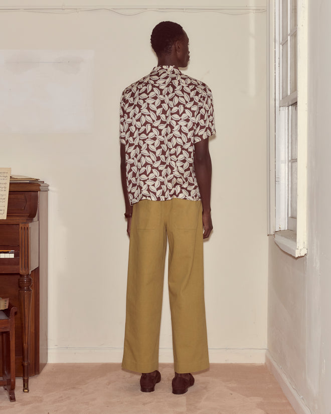 Indoors, a person faces a wall while wearing the Paper Birch Short Sleeve Shirt and tan pants.