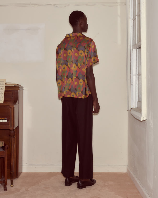 A person stands in the corner, back to the camera, wearing the Fruit Pit Short Sleeve Shirt paired with black pants.
