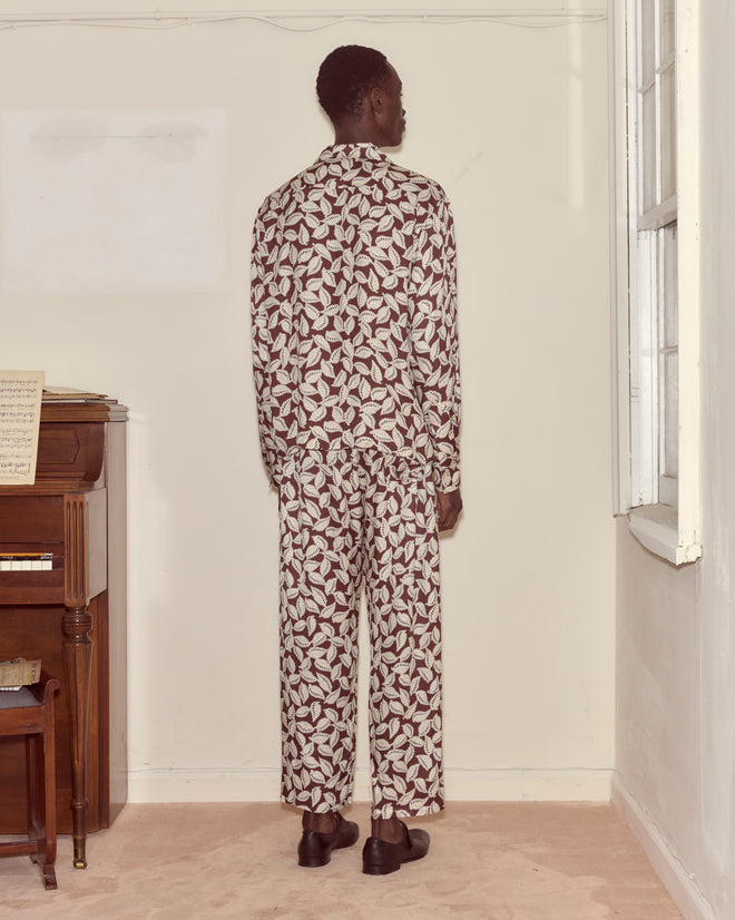 A person wearing a Paper Birch Long Sleeve Shirt stands facing a wall near a piano and window in a softly lit room.