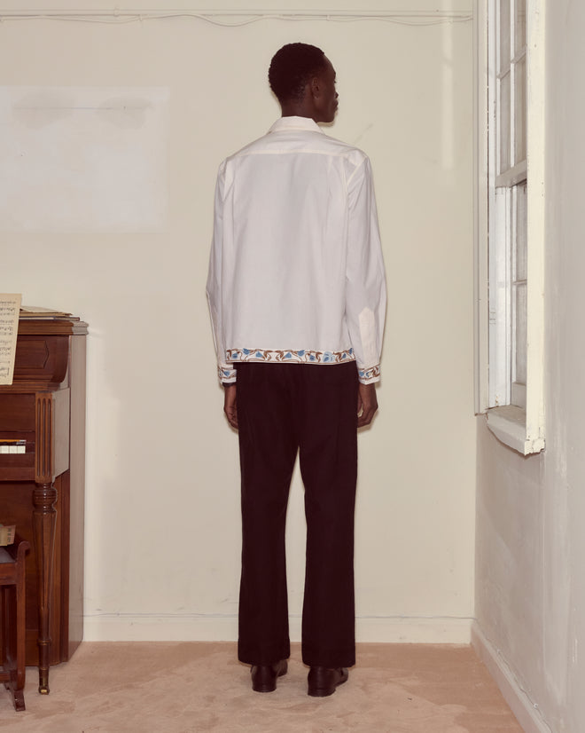 A man in the Nouveau Vine Long Sleeve and black pants stands facing a corner in a sparsely furnished room.
