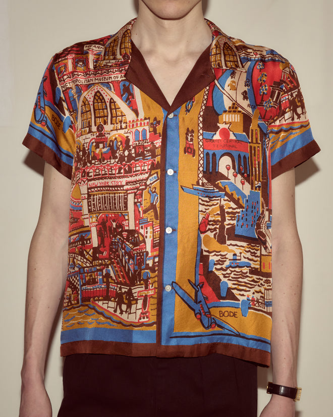 A person wearing the Manhattan Island Short Sleeve Shirt, featuring colorful, intricate cityscape patterns inspired by iconic Manhattan and Grand Central Terminal.