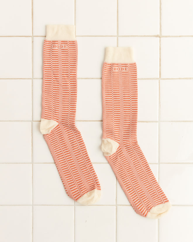 A pair of Micro Check Socks - Peach/Cream for children is displayed on white tiled flooring.