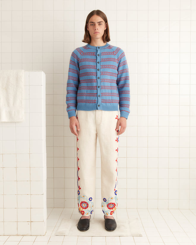 A person in a patterned blue sweater and the Beaded Garden Party Trousers, made from 100% linen, stands in a tiled room.