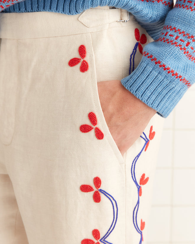 Someone is wearing Beaded Garden Party Trousers, crafted from 100% linen with red floral embroidery, paired with a blue patterned sweater.