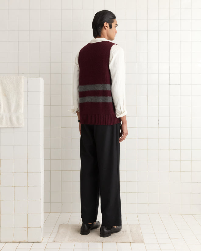 In a tiled room, someone in a 1950s-style Collegiate Vest in maroon and black pants stands facing away.