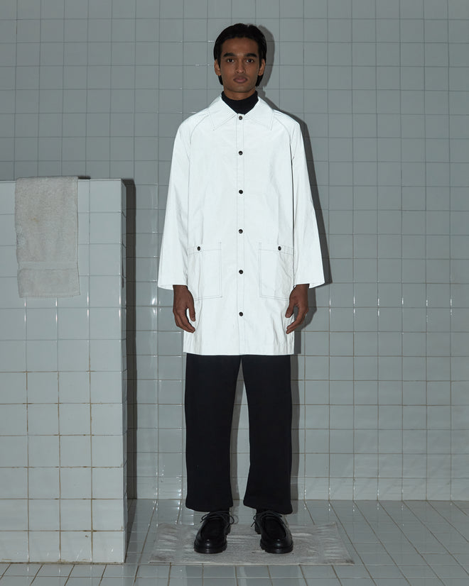 A person wearing a Reflective Rain Coat and black pants stands in a tiled room, with a towel placed on a tiled partition.