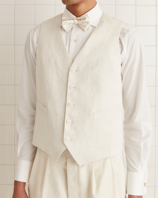 A person wearing the Nelson Brookline Waistcoat, styled in a cream linen suit and bow tie reminiscent of the 1940s-1950s, stands against a tiled background.