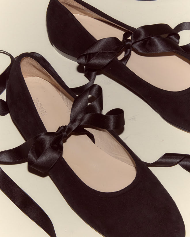 The Musette Flats - Black, featuring black ribbon ties, rest on a light surface and blend classic style with the elegance of leather shoes.