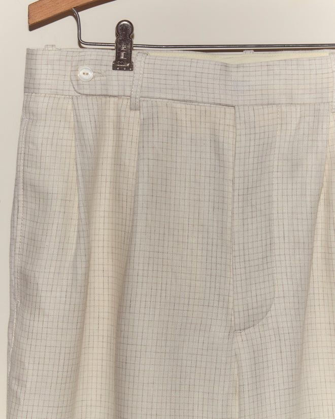 The Nelson Trousers - Ecru, featuring a subtle checkered pattern, hang on a hanger against a plain background, evoking classic 1950s style.