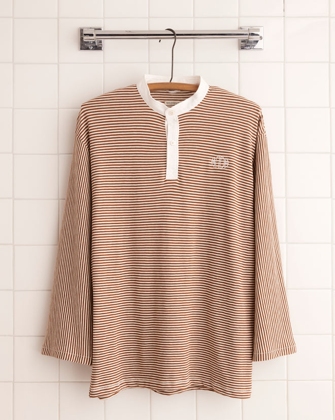 The Newton Stripe Polo - Brown, featuring striped brown and white long sleeves with a band collar, elegantly hangs against a tiled wall.