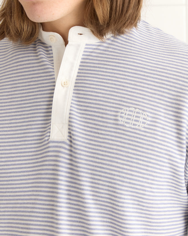 A person wearing a Newton Stripe Polo in blue, showcasing a monogram on the chest and a buttoned collar, echoing classic French polo style.
