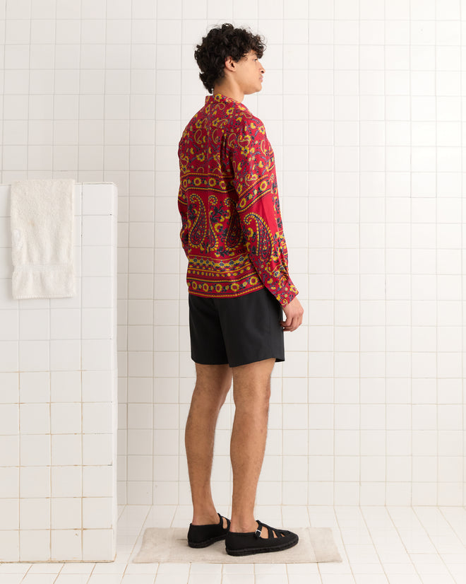 Person in a Cherry Paisley Long Sleeve Shirt, black shorts, and sandals stands sideways in a tiled room.