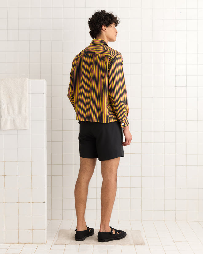 Person stands in a tiled room, facing away, wearing the Fish Appliqué Long Sleeve Shirt styled with black shorts and sandals.