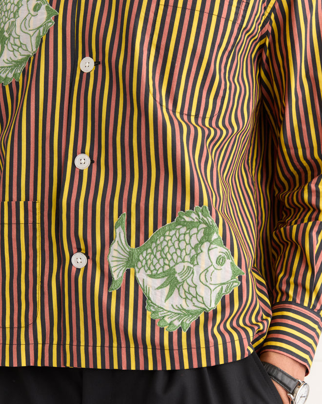 The Fish Appliqué Long Sleeve Shirt features green fish patterns and white buttons, channeling 1950s-1960s style, and is worn with one hand in the pocket.