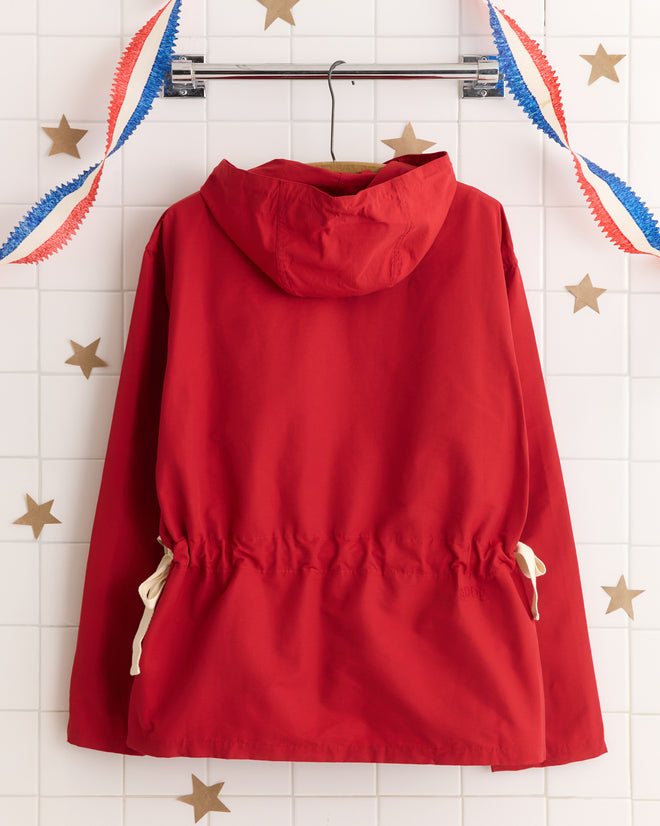A Nylon Tie Anorak - Red hangs on a rack, with star decorations and red, white, and blue streamers in the background.