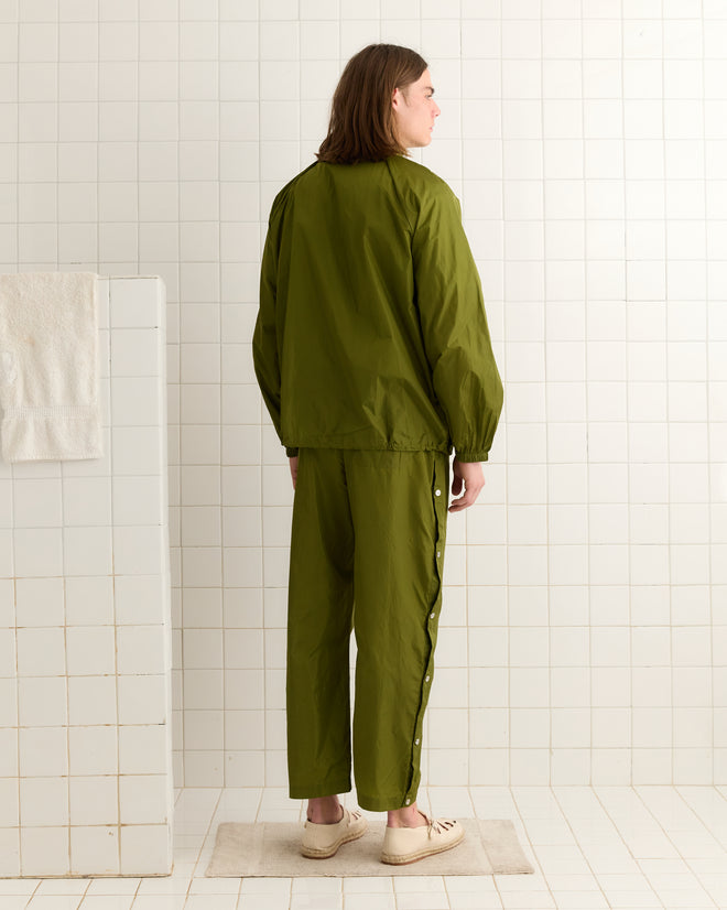 Someone wearing an olive Nylon Track Jacket stands facing away in a meticulously tiled room.