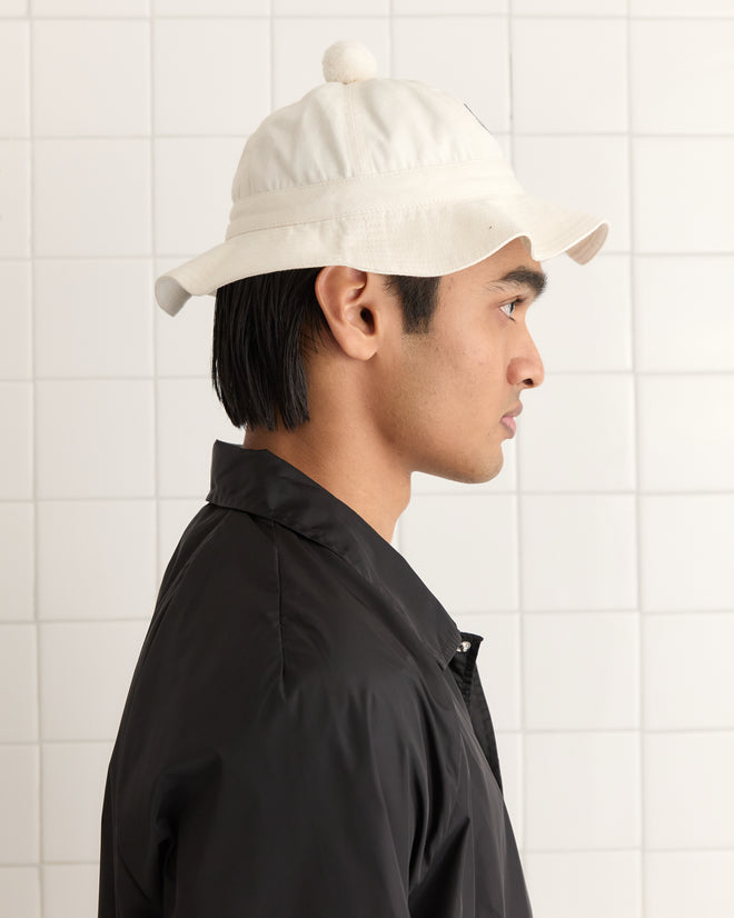 Person in profile wearing a crisp Paneled Grandfather Hat - White and a black jacket, standing against a tiled wall.