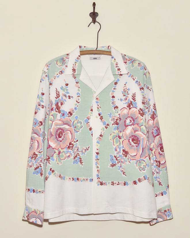 The Pastel Bouquet Long Sleeve Shirt - L/XL, featuring a unique pastel floral print, hangs on a hook against a cream wall, bringing a touch of midcentury charm.