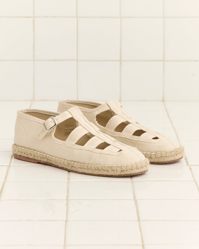 Peggy Espadrilles - Natural, featuring a canvas upper with cutout sides, buckle straps, and a classic jute sole, are shown on a white tiled surface.