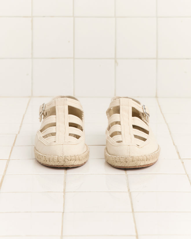 The Peggy Espadrilles - Natural, a pair of beige jute sandals ideal for summer leisure, are shown from the back on a white tiled floor.