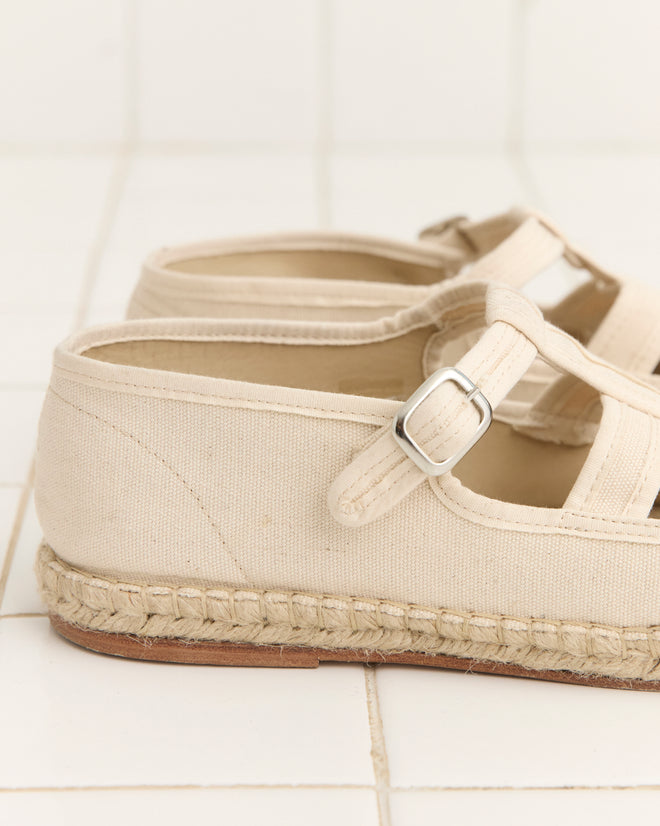 The Peggy Espadrilles - Natural feature beige canvas, buckle straps, and woven jute soles, resting on white tiles—perfect for effortless summer style.
