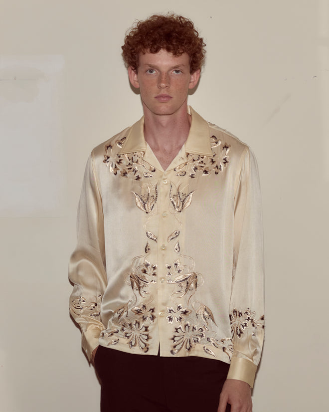 A man with curly hair wears the Phantasm Long Sleeve Shirt in ivory silk with Victorian embroidery and dark pants, standing against a plain background.