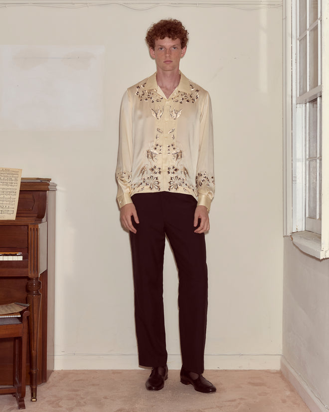 A person in a Phantasm Long Sleeve Shirt and black pants stands indoors beside a piano and a window.