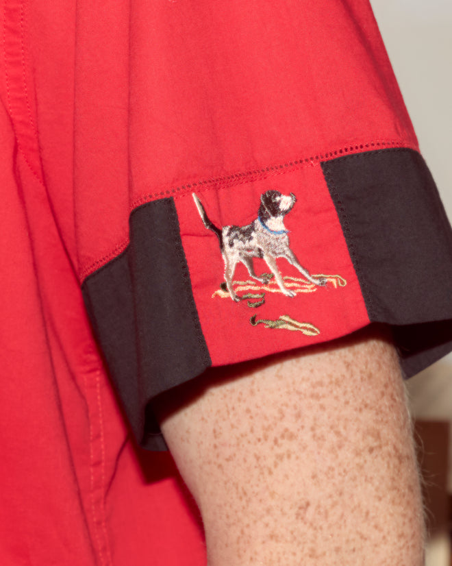 The Pointer Short Sleeve Shirt features red cotton fabric, black trim, ladderwork details, and an embroidered dog motif on the cuff.
