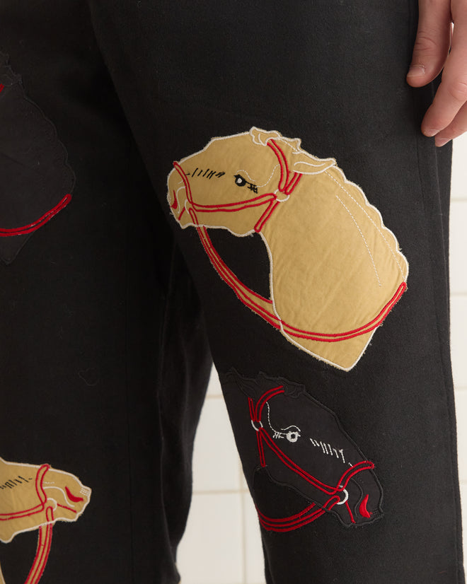 Pony Appliqué Trousers in black, featuring horsehead designs in beige and red, with a hand on the hip.