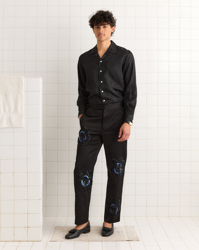 A person stands in a tiled room wearing black button-up shirt and Poppy Suiting Trousers - Black.