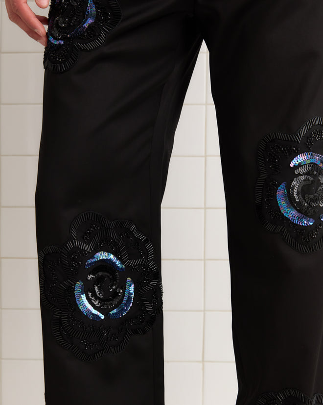 Poppy Suiting Trousers - Black, featuring shiny black and blue satin weave floral patches, displayed against a tiled background.
