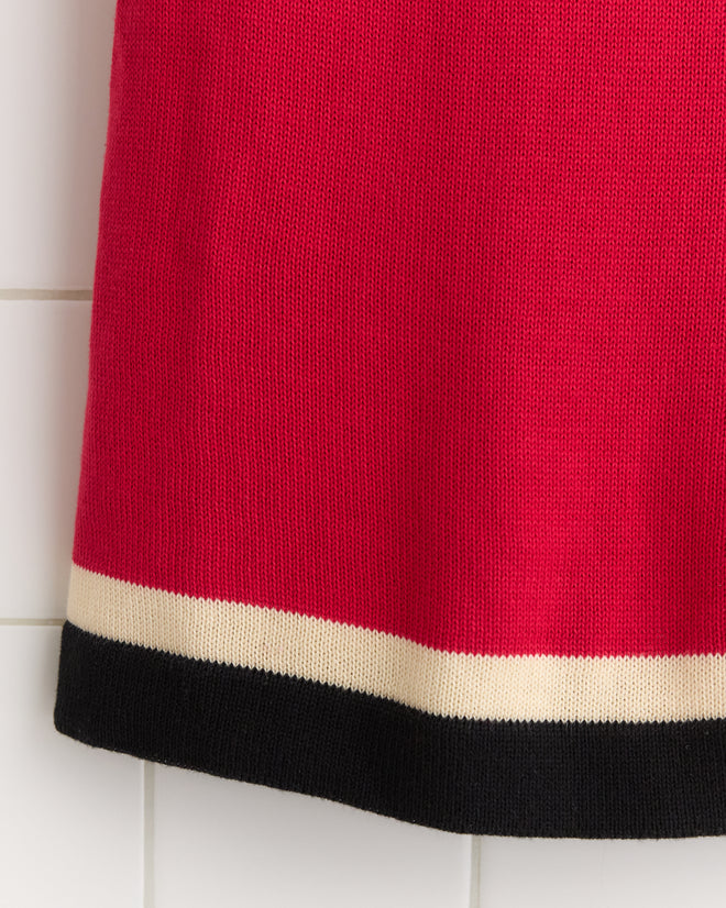 The Port Dress, featuring red fabric with cream and black stripes at the hem, evokes a 1900s–1920s rowing singlet and is displayed against a white tiled background.