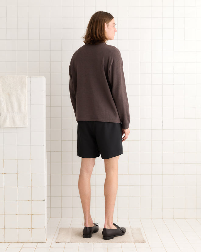 Wearing the Port Polo in its brown and black design, a person stands in a white tiled room, facing away from the camera, as if preparing for an adventure to Port Renfrew.
