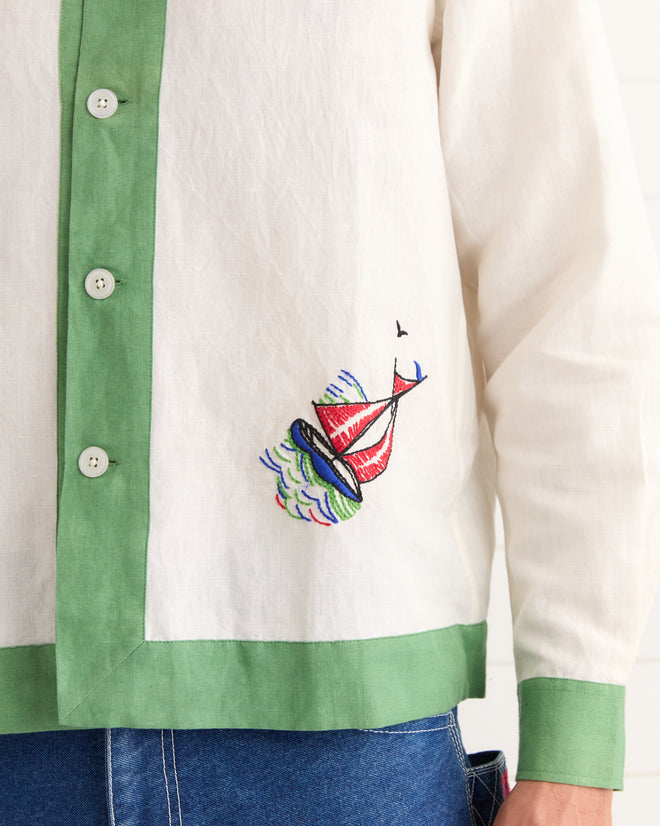 The Primary Sailboat Long Sleeve Shirt - Green Cream features green trim and colorful sailboat embroidery near the hem, styled with classic blue jeans.