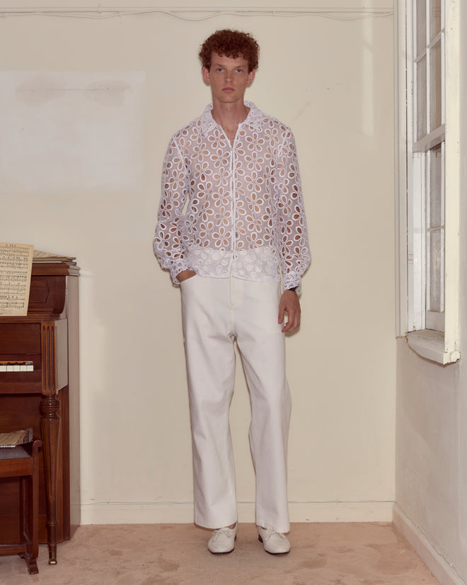A man in a Primrose Lace Long Sleeve Shirt and white pants stands indoors beside a piano and a window.