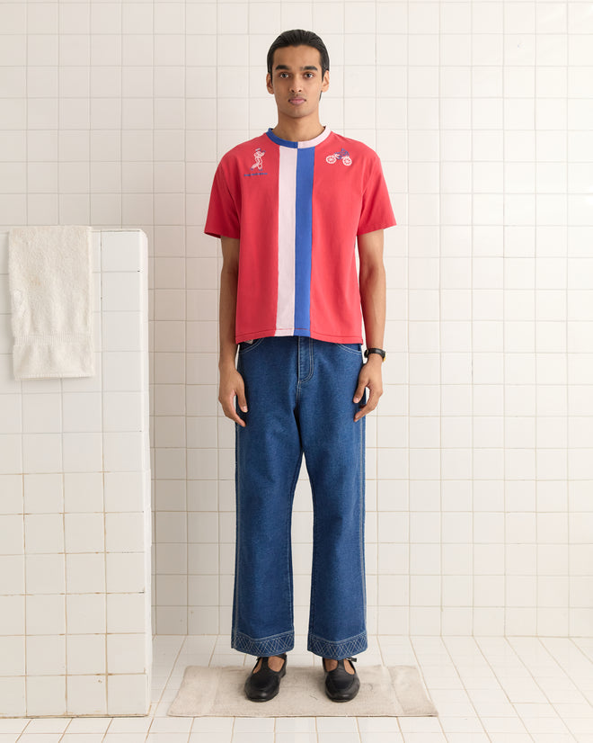 A person in a Racing Stripe Tee and jeans stands on a bath mat in a tiled room, with a towel draped over the partition.