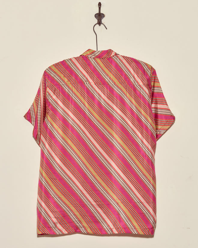 The Railhead Blooms Shirt - M/L, featuring pink, white, and beige diagonal stripes, hangs on a wall hook.
