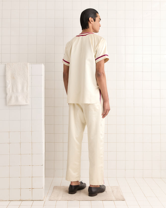 A person in a Redtail Baseball Shirt stands on a vintage 1960s-style rug in a tiled bathroom, facing away.