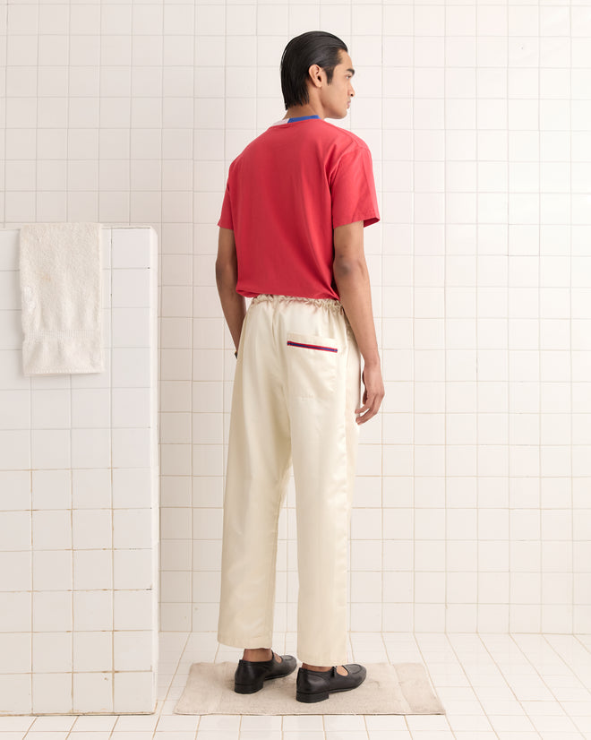 A person wearing a red shirt and Redtail Pajama Pants is standing in a tiled room, with a towel hanging nearby.