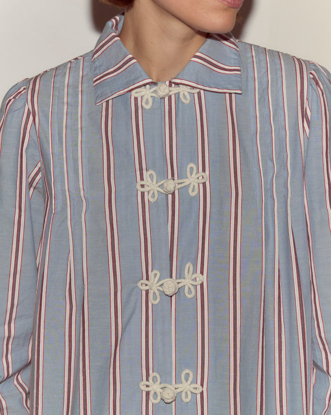 A person wearing the Regatta Stripe Jonas Shirt, a 1930s-inspired design with blue fabric, red and white stripes, knotted white buttons, and an antique City of Paris label.