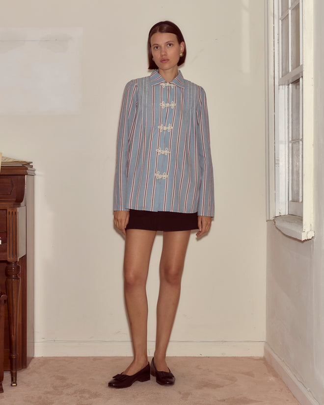 A woman wearing the Regatta Stripe Jonas Shirt and a black skirt stands indoors by a piano and window, looking at the camera.