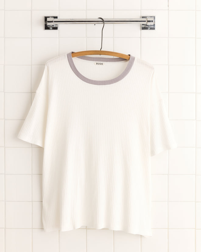 The Rib Boxy Tee, a vintage white T-shirt crafted from 100% cotton, features a stylish grey ringer neckline and hangs on a wooden hanger against the tiled wall backdrop.