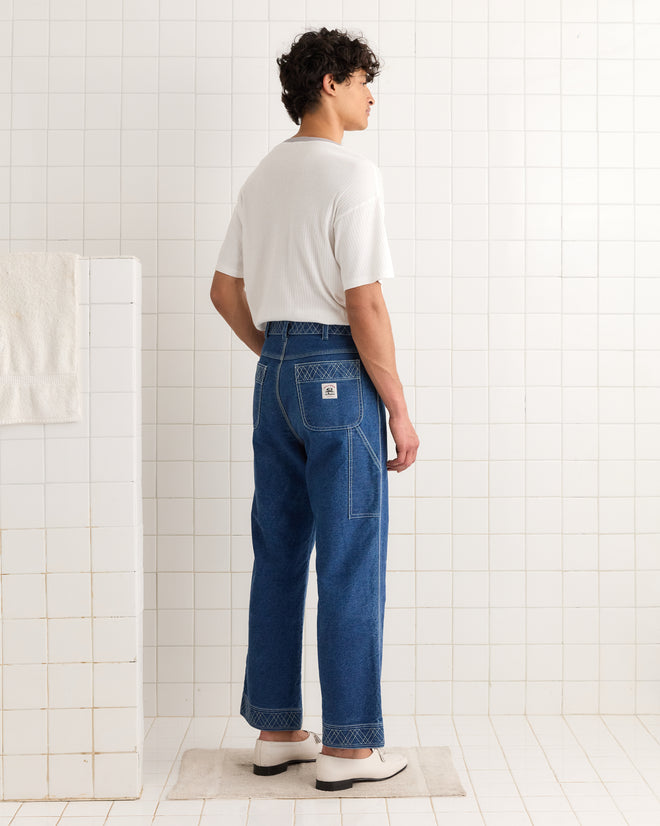 A person stands on a mat in a tiled room, wearing a white Rib Boxy Tee and blue jeans, facing away.