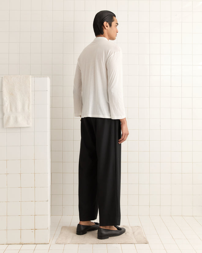 A person in a Salt Marsh Polo and black pants stands in a tiled room, facing away. A towel hangs on a nearby wall.
