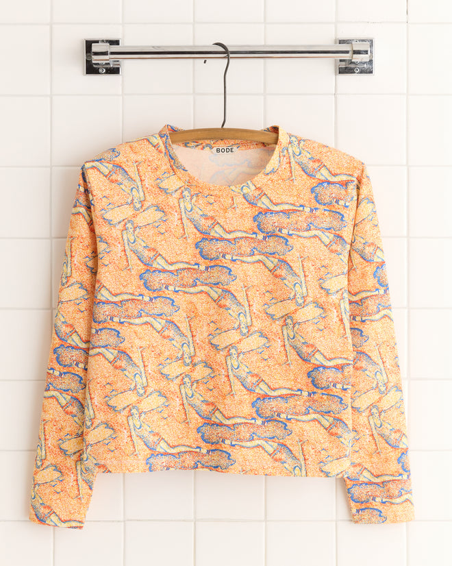 A Sandbank Long Sleeve Tee with a swirling abstract design, reminiscent of pointillism, hangs elegantly on a hanger against a tiled wall.