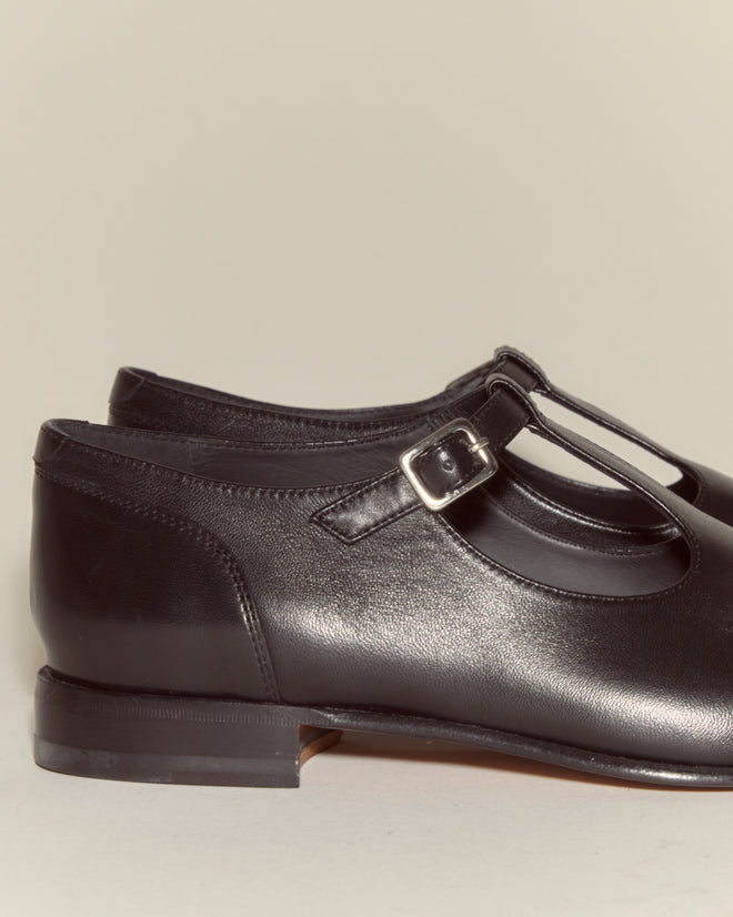 School Shoes - Black: Italian-made black leather T-strap shoes with a side buckle, displayed on a neutral background.