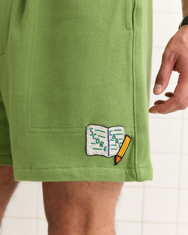 A close-up of Score Card Shorts—green Canadian rugby shorts featuring a playful open notebook and pencil patch near the hem, adding a novelty golf-inspired twist.