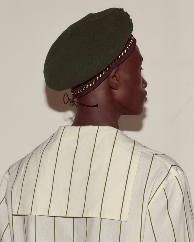 Person wearing the Script Beret - Green with Brown/Black Piping, made in France from 100% wool, and a striped shirt, shown from behind against a plain background.
